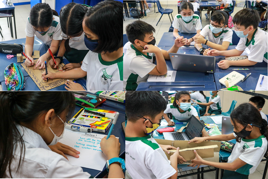 Students wearing masks work in groups in a classroom, writing, using laptops, and building with cardboard.